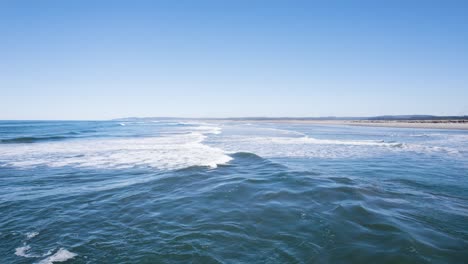 Side-view-following-rolling-waves-along-Bandon-Oregon-coastline-on-sunny-day