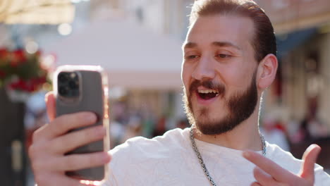 Excited happy winner young man use smartphone celebrating win good message news in city street