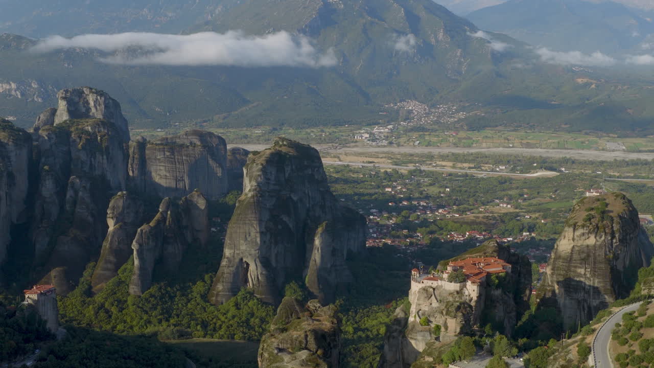 Cinematic aerial view of Meteora monastery in Greece perched on towering cliffs, dramatic rock formations and lush green valley create a breathtaking historic scene