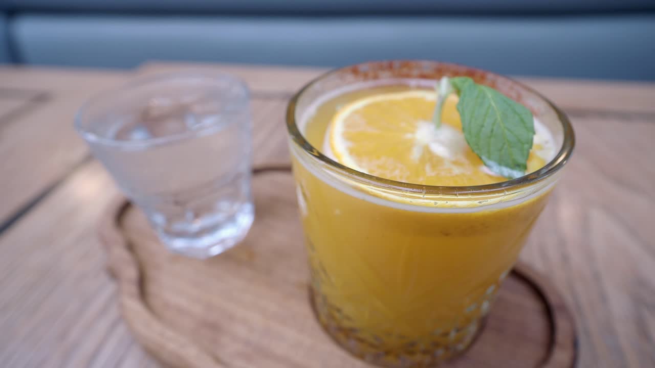 Primo piano di un bicchiere di succo d'arancia con una fogliolina di menta e una fetta d'arancia in cima
