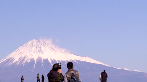 espalda de personas tomando fotos del monte fuji, mostrando la escala de la montaña