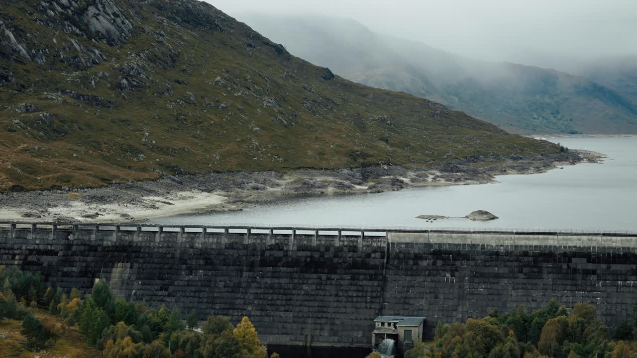 Aerial pan up of Loch Cluanie dam against mist-covered Highlands, Scotland