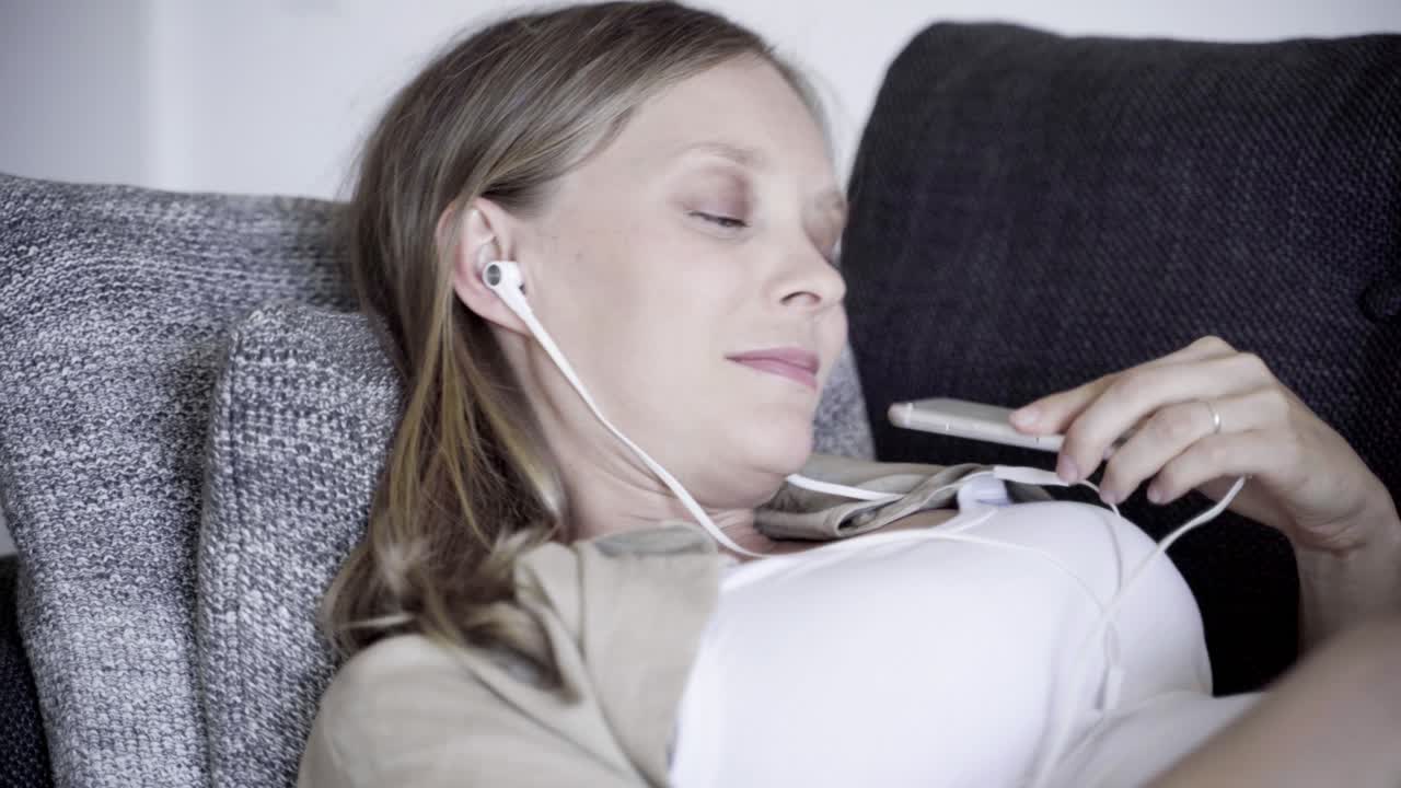 편안 한 임신 한 여자 가 소파 에서 음악 을 듣고 있다