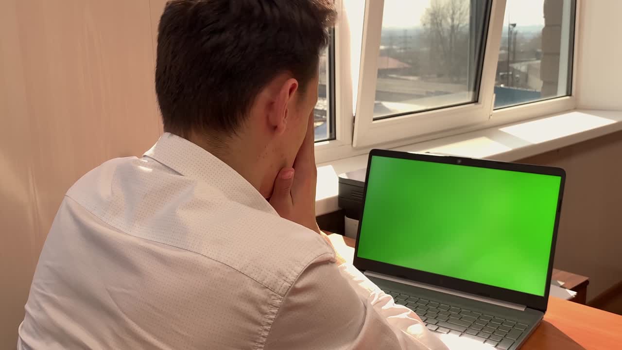 un hombre caucásico frustrado se sienta en un escritorio frente a una computadora con una pantalla verde en la oficina y se frota la cara con las manos. adicto al trabajo, trabajo duro, escalera de carrera, ganar dinero