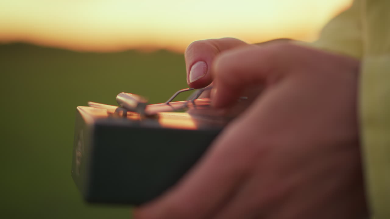 hands plucking kalimba at golden hour, white busker improvises lively thumb piano melody in open field with warm sunset glow and soft bokeh, closeup of thumbs and levers showing tactile rhythm