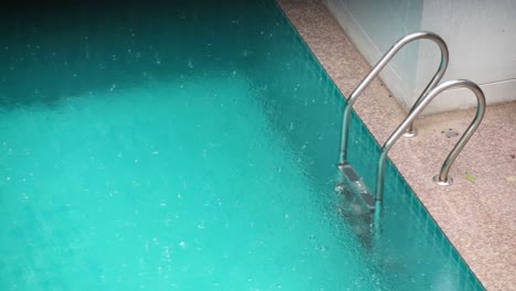 close up of swimming pool with ladder with rain falling heavily in thailand