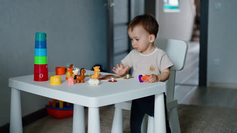 smart little kid playing with toy animals on the white table. boy toddler stands up and walks around the desk.