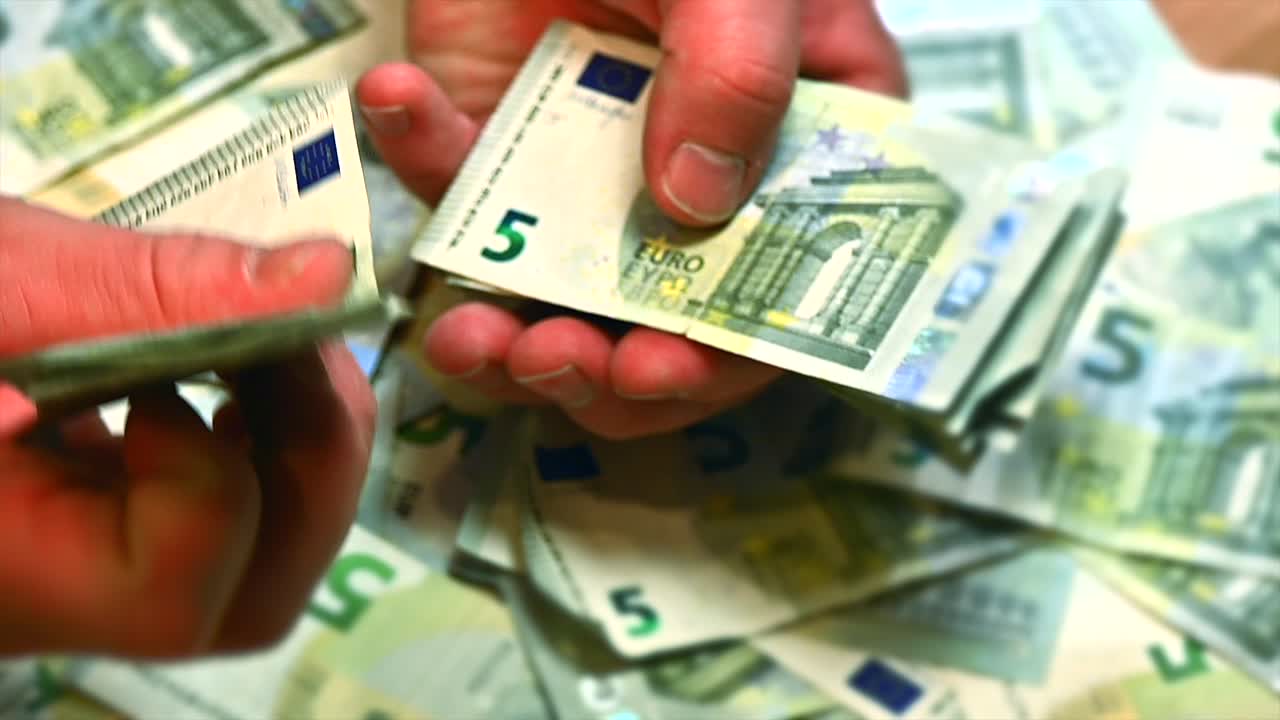 Hender av en kaukasisk mann som blar gjennom et hav av 5-eurosedler, makrobilde.