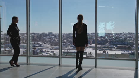 beautiful lady standing at the window and looking through it. another lady comes and points at something outside the window.