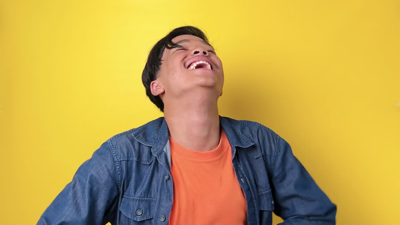 캐주얼 스타일의 아시아 젊은이가 노란색 바탕에 고립되어 큰 소리로 웃습니다.