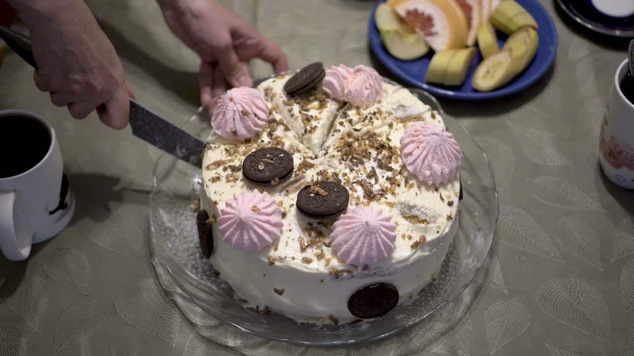한 여자가 마쉬멜로와 초콜릿으로 장식된 아름다운 생일 케이크를 조각으로 잘라서 유리판 위에 놓습니다.