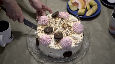 una mujer corta en pedazos un hermoso pastel de cumpleaños decorado con malvaviscos y chocolate, que se encuentra en una bandeja de vidrio. fiesta en casa. concepto. primer plano. la vista desde la parte superior. 4k.