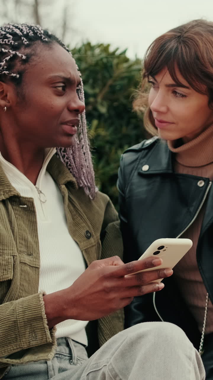Two Young Diverse Women Discussing Content on a Smartphone Outdoors