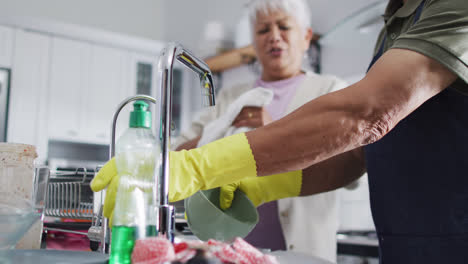 happy senior biracial couple washing dishes in kitchen