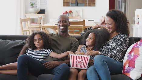 family sitting on sofa at home eating popcorn and watching movie together