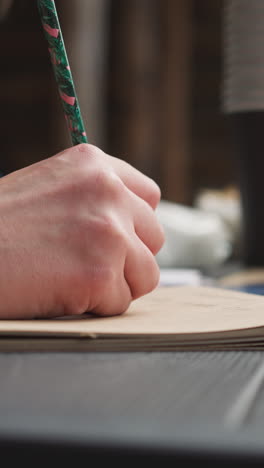 woman writes in notebook sitting at table in courtyard with wooden buildings. screenwriter takes notes being at place of historical events on blurred background closeup