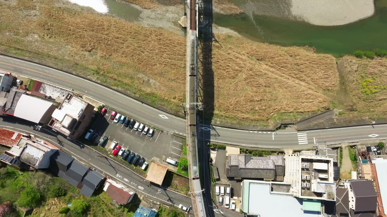 Aerial drone follows a train, railway in motion crossing a Japanese river during Cherry blossom spring Landscape, local village