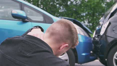 young male motorist with whiplash injury in car crash sitting next to damaged vehicle