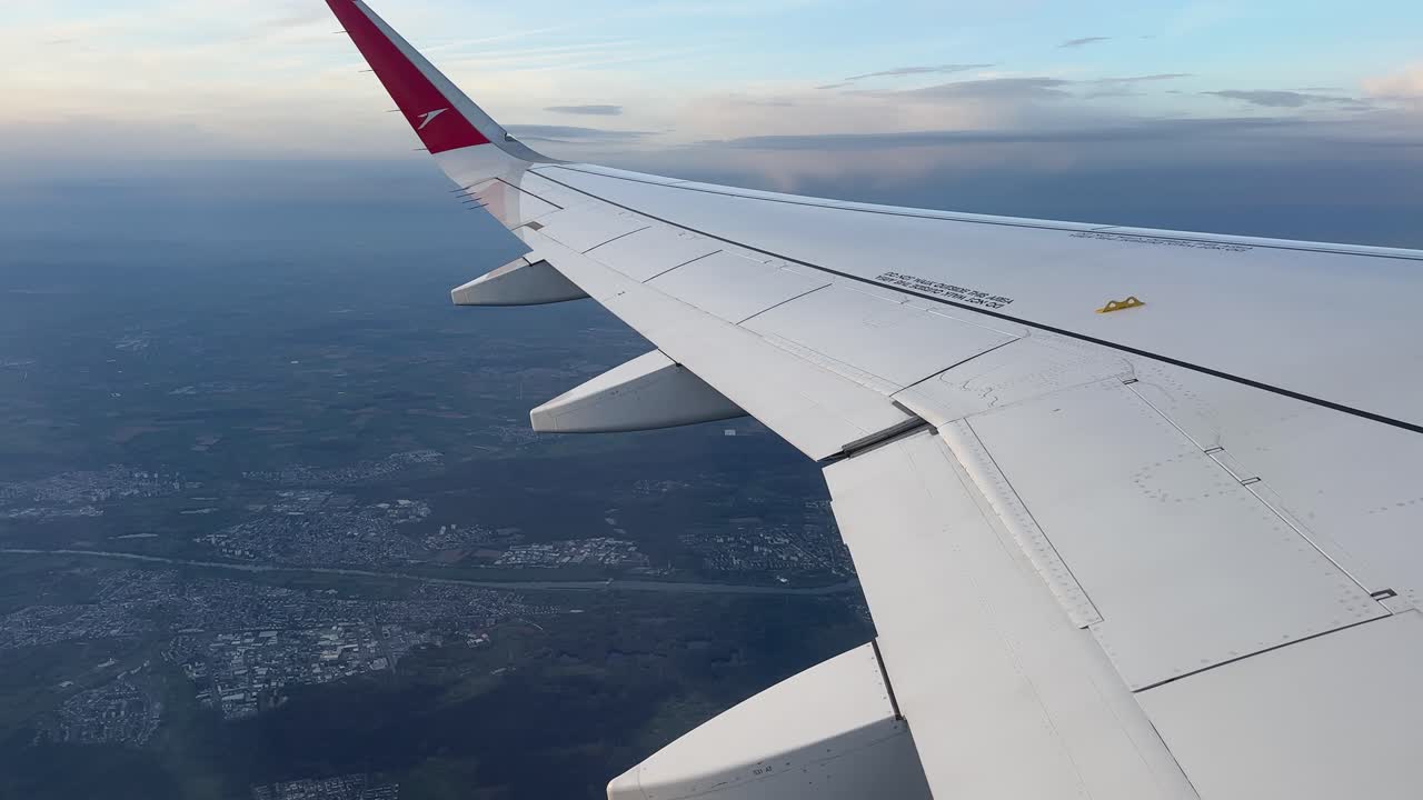 Vista dall'ala dell'aereo durante il volo su Francoforte con il paesaggio urbano sottostante e un orizzonte con cielo serale tenue.