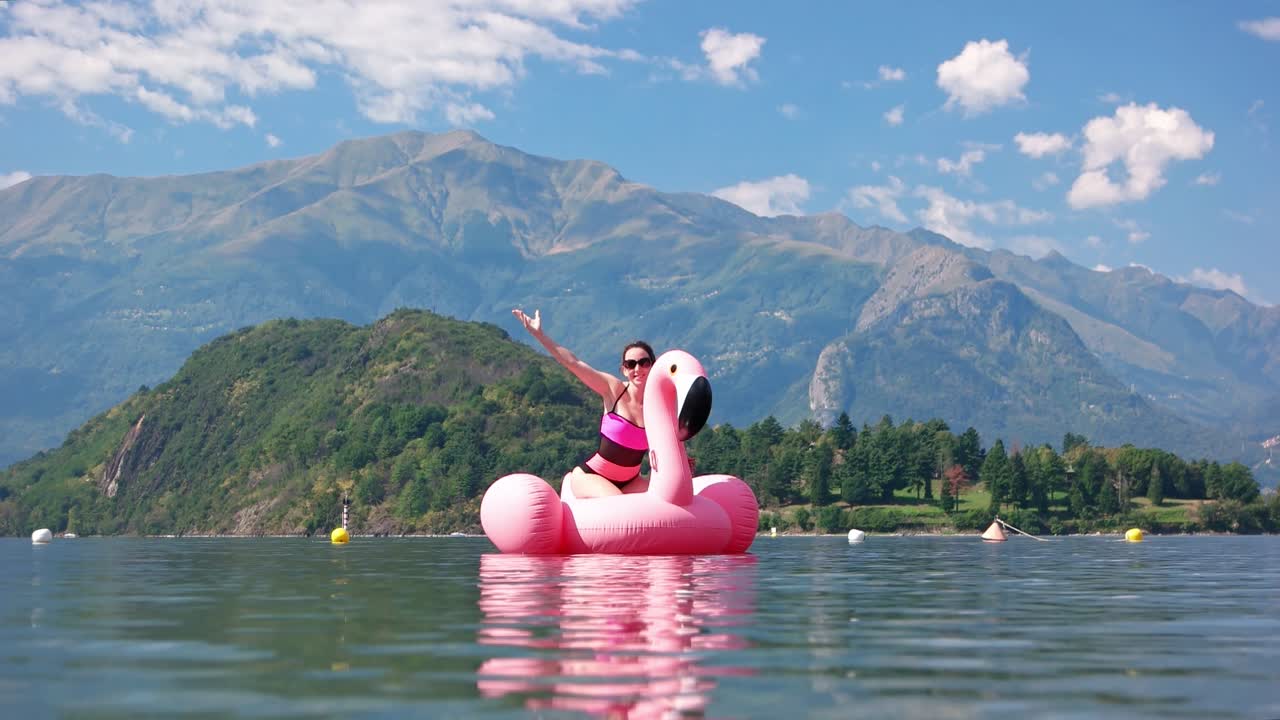 video de una mujer montando en un flamenco inflable en el lago como con el impresionante fondo de las montañas circundantes. capturas de un día soleado de verano con algunas nubes escasas.