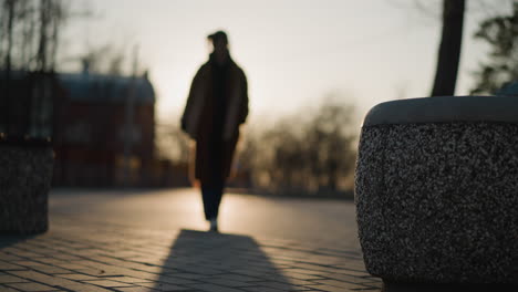 in a park at sunset, the silhouette of a person walking slowly in grief is visible, with the background and foreground both blurred, creating a soft, somber atmosphere