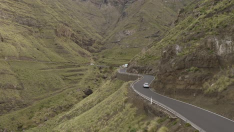 drone shot of a car driving through a curvy road in a canyon with mountains