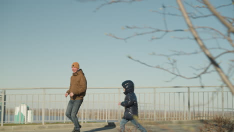 close up of father and son running on a bridge happily with a cityscape in view and a branch of tree