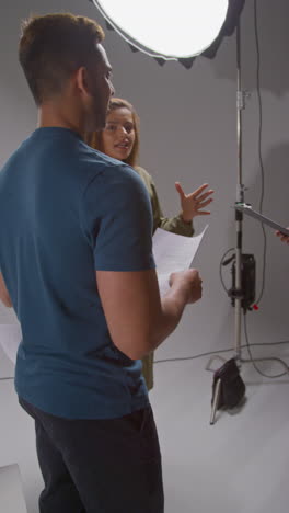 vertical video of film director talking with male and female actors holding scripts rehearsing for shooting movie or video in studio 6