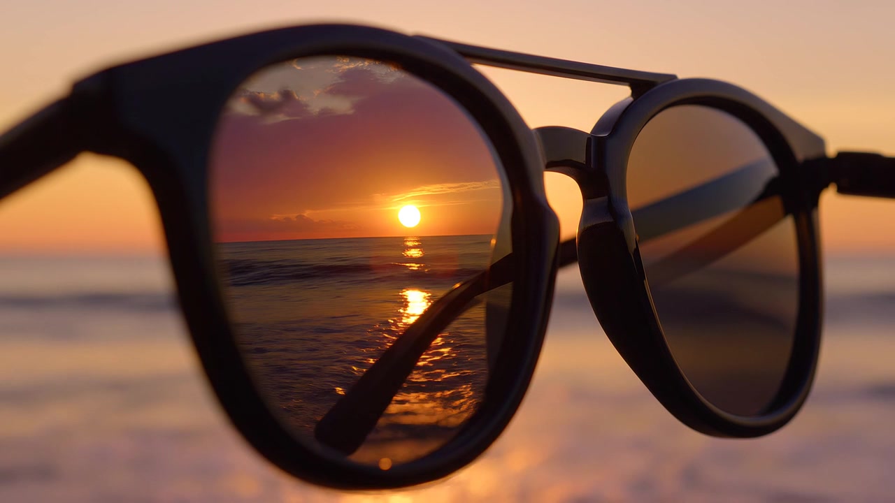 Reflejo de la puesta de sol en gafas de sol de montura negra en una playa