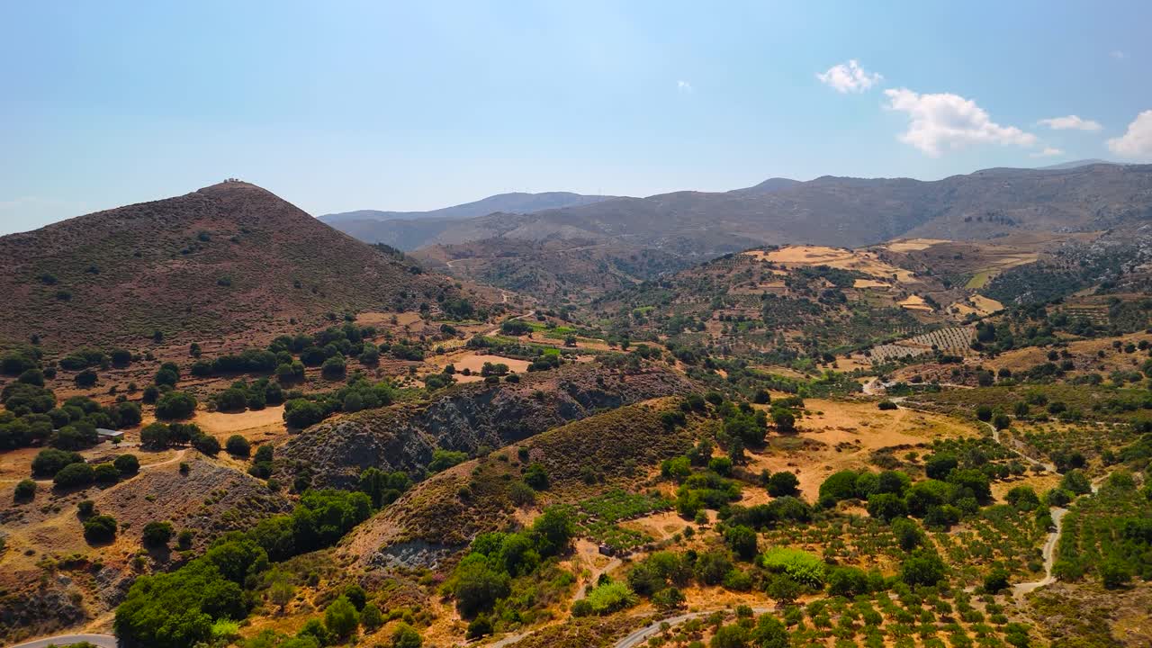 This breathtaking landscape shows rolling hills, winding roads, and lush greenery under a clear sky in southern Greece, capturing a serene afternoon atmosphere