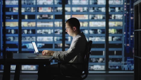 businessman returning to office opening laptop lid and continue in evening work. handsome caucasian man against night city scene in background.