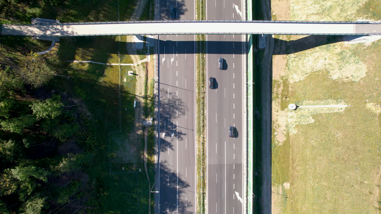 Drone bird's eye view rises above multi lane highway next to coniferous forest and grassy hill