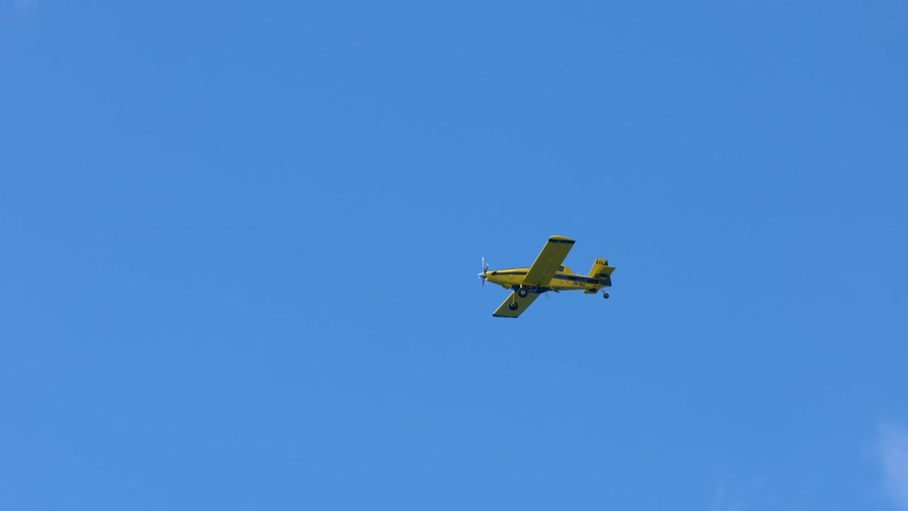 Un aereo agricolo giallo vola attraverso un cielo azzurro brillante con nuvole bianche