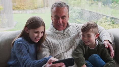 abuelo jugando videojuegos con los nietos en el teléfono móvil en casa