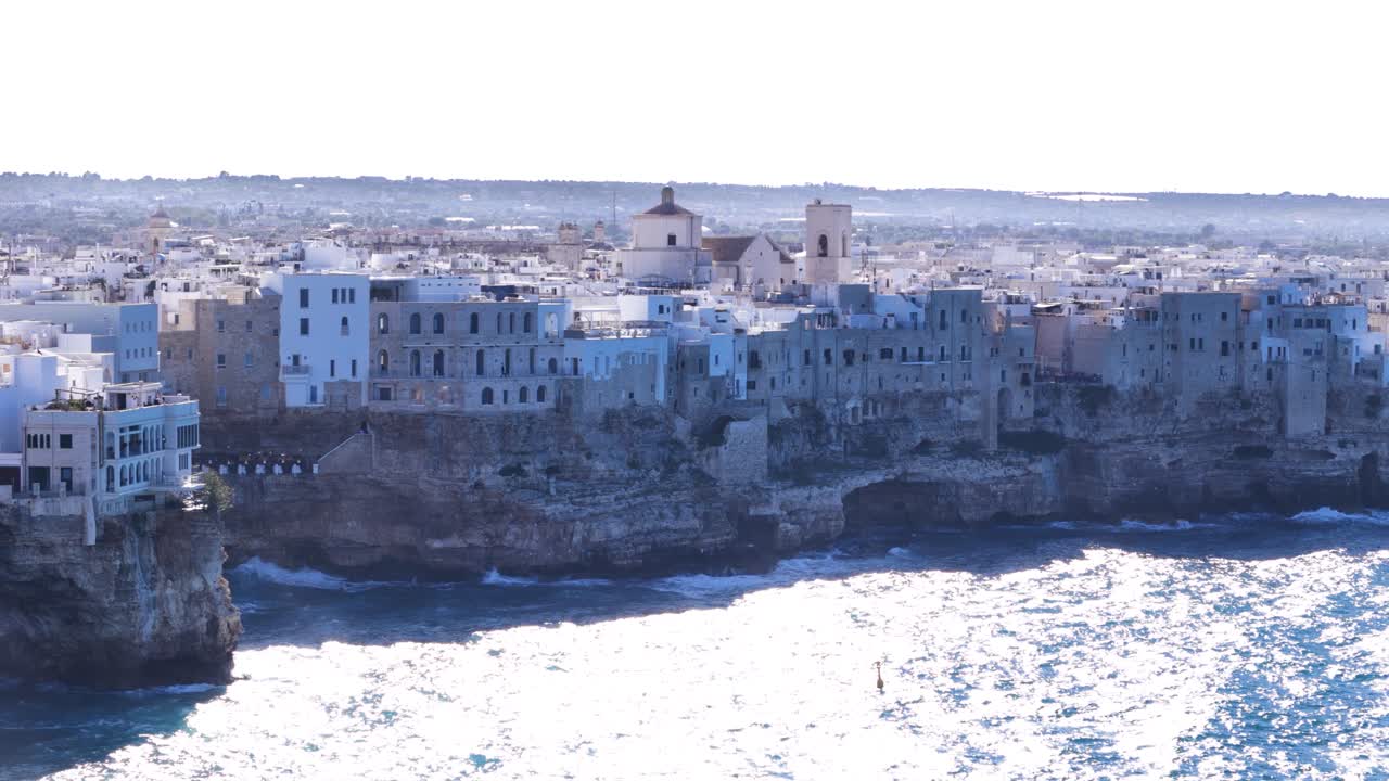Powerful waves hitting rocky cliffs with township of Polignano a Mare on top, aerial view