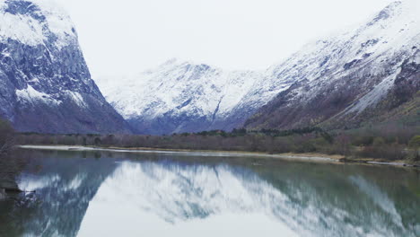 pintorescas montañas nevadas de trollveggen reflejadas en un lago claro en noruega - toma aérea