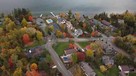 Aerial-truck-pan-passing-over-the-houses-of-a-residential-neighborhood-along-a-river,-trees-are-vibrant-with-autumn-colors-as-the-season-changes,-Canada