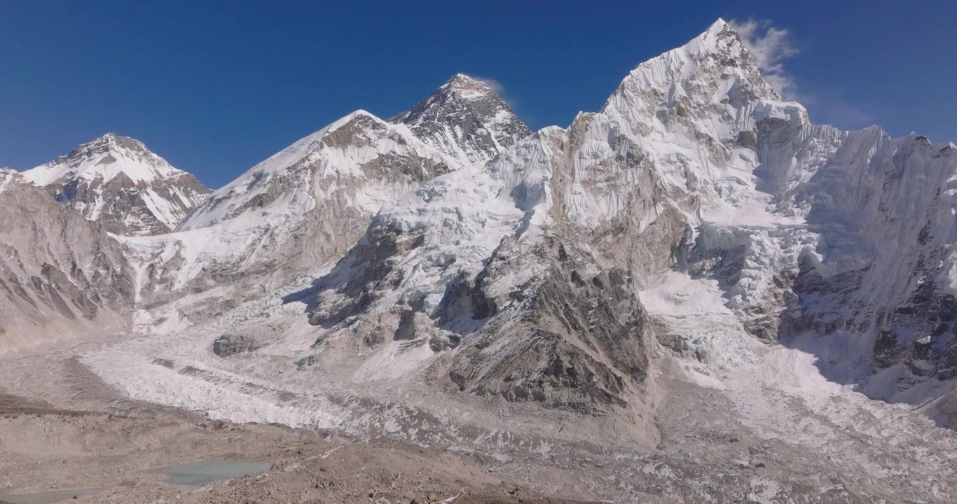 Kala Patthar Campo Base Everest Nepal, drone che sorvola una scura cresta rocciosa per rivelare le imponenti cime innevate del Monte Everest e del Nuptse che si ergono contro un cielo blu intenso
