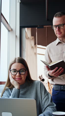 office teammates look at laptop discussing work. colleagues consulting, advising and helping each other. lunch time at workplace. vertical video