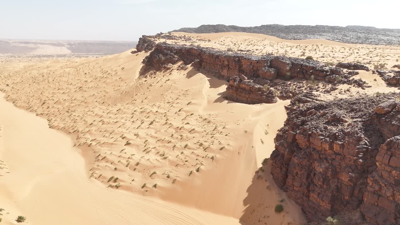 Aerial drone view of golden Sahara desert dunes meeting dark rocky cliffs in Mauritania, dramatic contrast of sand and stone in the remote wilderness