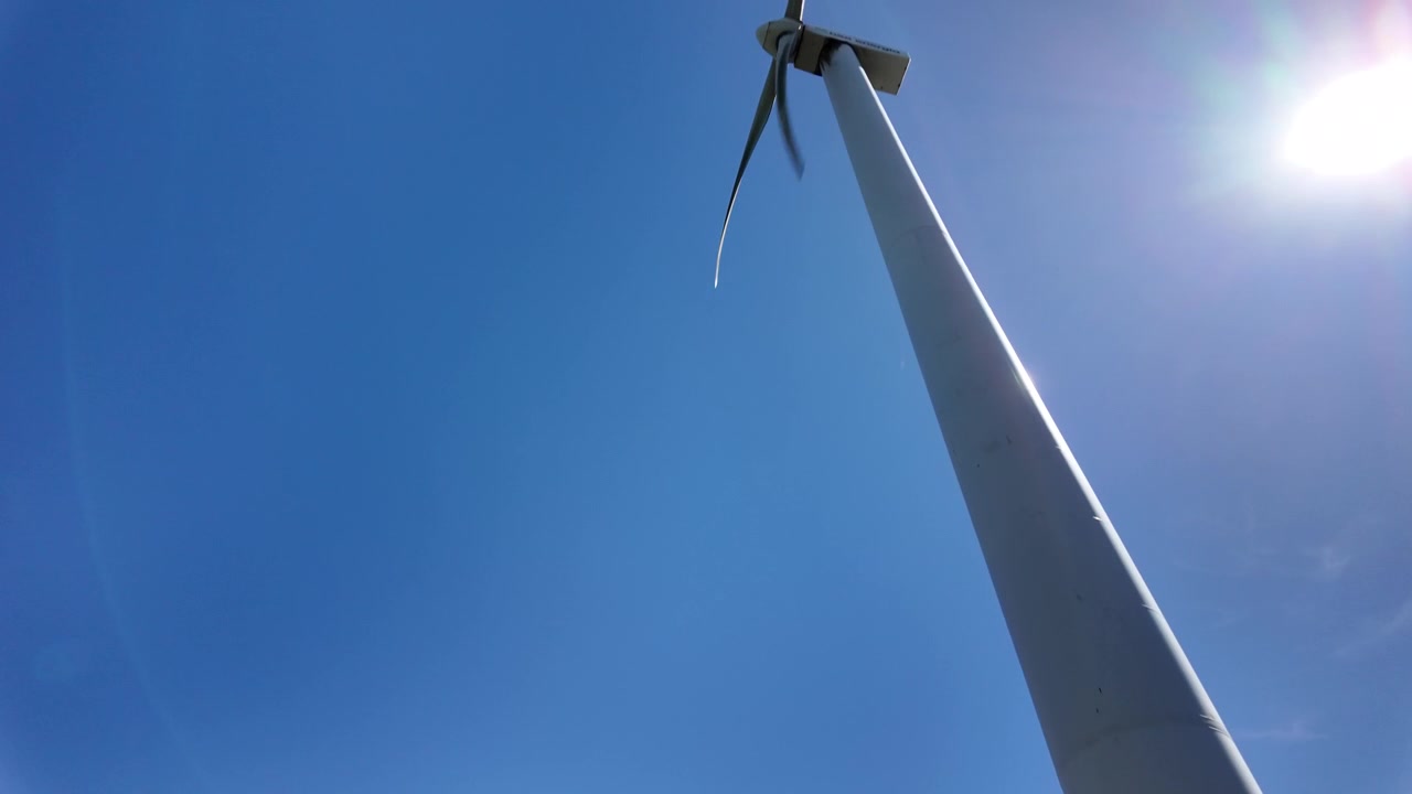 Vista in slow motion dal basso di una turbina in rotazione su una collina costiera.