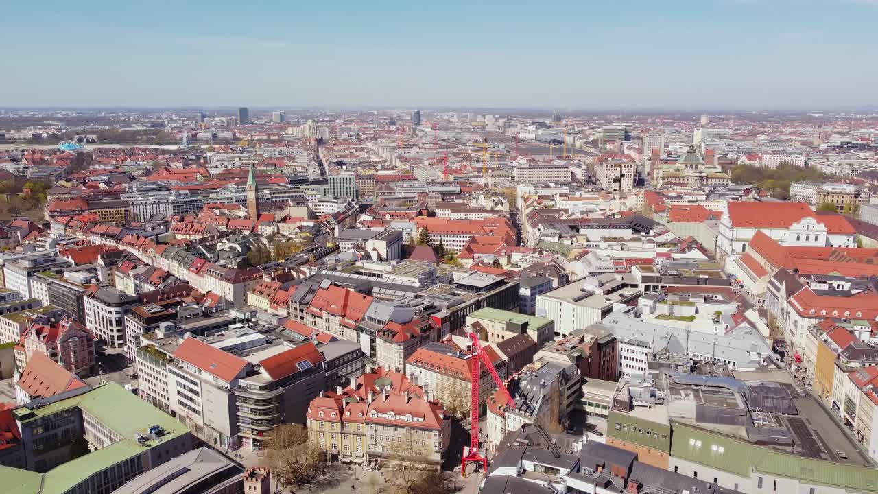 Wide aerial perspective of Munich, Germany, showing the dense red-roofed historic architecture and city grid, captured from above during a bright spring day over Marienplatz area.