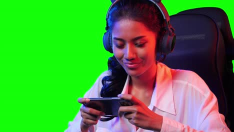 esports gamer mujer jugando juegos en línea en el teléfono inteligente en casa. mujer asiática controlando la consola con teléfono inteligente en el videojuego. mujer joven juego de ocio en la sala de estudio y pantalla verde en casa.
