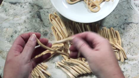 vista aérea de las manos abriendo fideos de masa de pasta y agregando en un tazón blanco