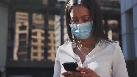 Mujer-Afroamericana-Con-Máscara-Facial-Usando-Un-Teléfono-Inteligente-En-La-Calle