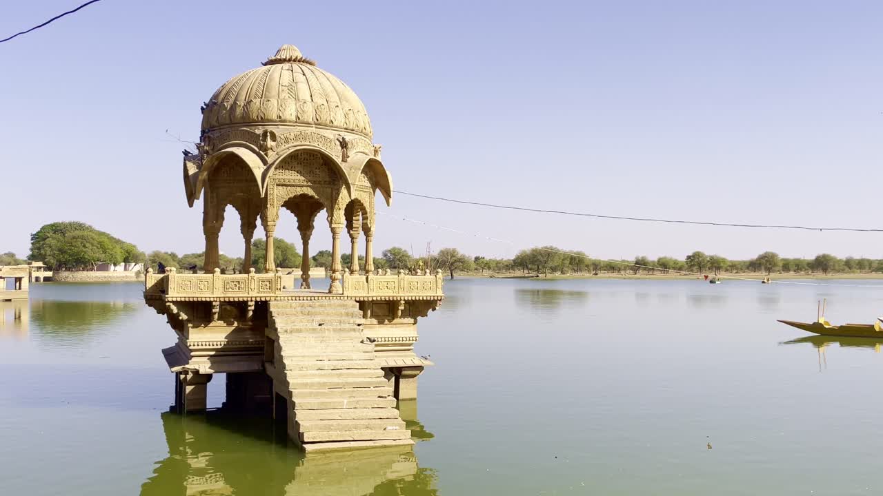 Gadsisar Lake in Jaisalmer sparkles under the Rajasthan sun, mirroring ancient temples and peaceful pavilions. Calm waters, migratory birds, and golden hues enhance its timeless desert beauty India