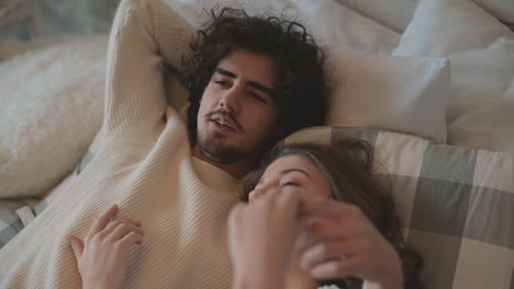 close up of young romantic cute couple lying in bed talking in love and wearing winter clothes