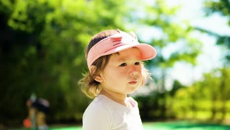 Retrato-De-Una-Bonita-Cara-De-Niña-Pequeña-Mirando-A-Un-Lado-Al-Parque-Contra-árboles-Verdes-Borrosos-En-Un-Día-Soleado