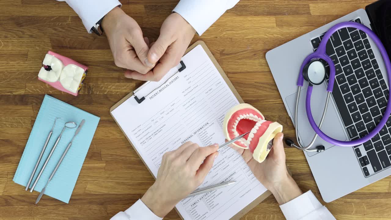 Overhead view of a dentist explaining dental hygiene to a patient using a dental model during a consultation