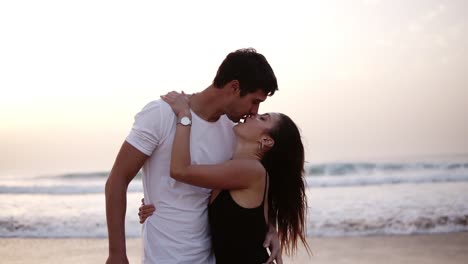 Couple-of-lovers-man-and-woman-paint-with-their-feet-on-the-wet-sand-heart.-Caucasian-loving-couple-on-the-sea-coast-kissing-in-front-the-ocean,-wearing-casual-clothes.-Front-view